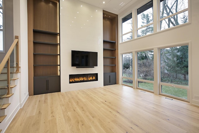 unfurnished living room featuring built in shelves, a large fireplace, light wood-type flooring, and a high ceiling