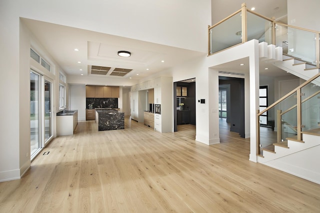 unfurnished living room featuring recessed lighting, light wood-style flooring, stairway, a towering ceiling, and baseboards