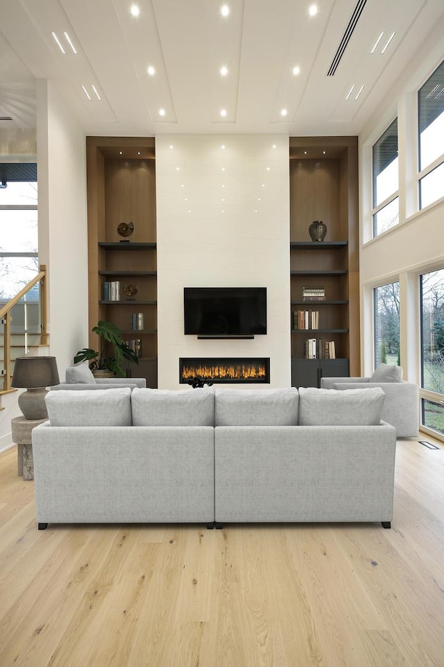 living room with light wood-type flooring, built in shelves, a fireplace, and visible vents