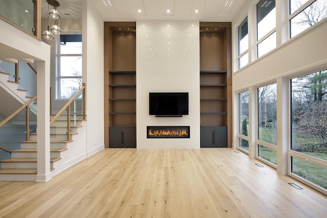 unfurnished living room with a towering ceiling, built in shelves, wood finished floors, and visible vents