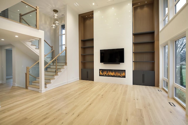 unfurnished living room with a large fireplace, wood finished floors, a towering ceiling, built in features, and stairway