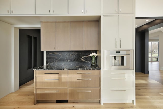 kitchen with light wood finished floors, tasteful backsplash, dark stone counters, and oven