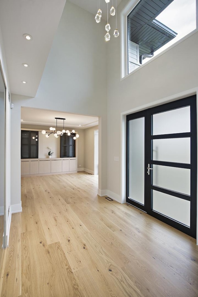 foyer entrance featuring a notable chandelier, recessed lighting, a towering ceiling, wood finished floors, and baseboards