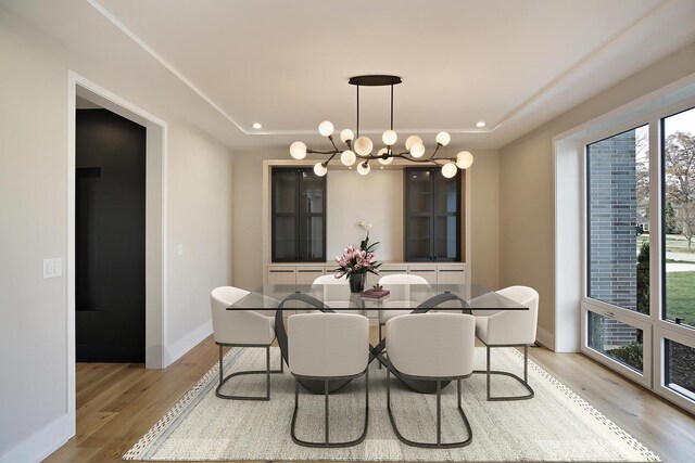 unfurnished dining area with a notable chandelier, a tray ceiling, and light hardwood / wood-style flooring