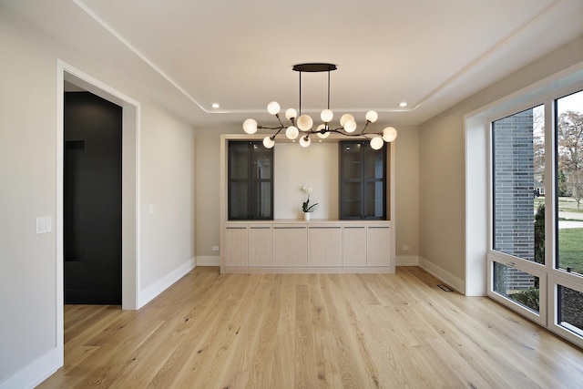 unfurnished dining area featuring a notable chandelier, light wood-style flooring, and baseboards