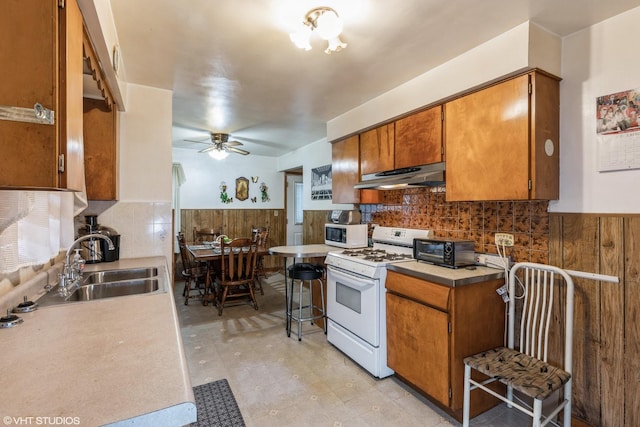 kitchen with decorative backsplash, white appliances, ceiling fan, sink, and a breakfast bar area