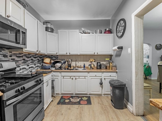 kitchen featuring white cabinets, appliances with stainless steel finishes, light hardwood / wood-style floors, and decorative backsplash