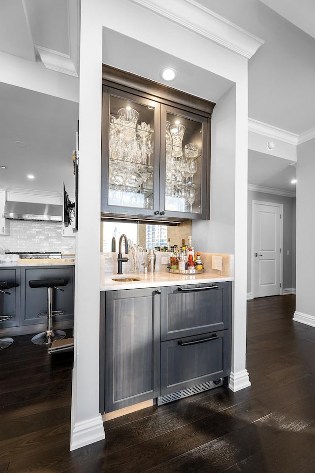 bar featuring sink, dark wood-type flooring, range hood, backsplash, and ornamental molding