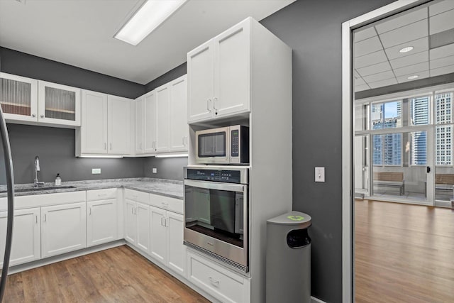 kitchen with light hardwood / wood-style floors, white cabinetry, light stone countertops, and appliances with stainless steel finishes