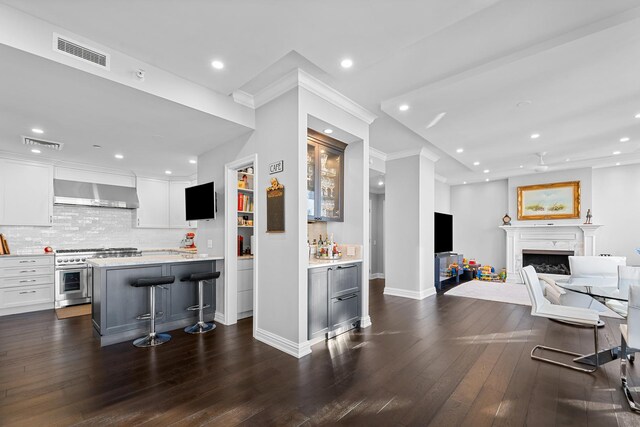 kitchen featuring dark hardwood / wood-style flooring, wall chimney exhaust hood, high end stove, white cabinets, and a breakfast bar area