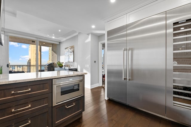 kitchen featuring dark wood-type flooring, crown molding, light stone countertops, appliances with stainless steel finishes, and dark brown cabinetry