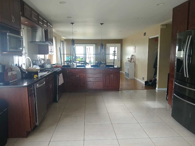 kitchen featuring kitchen peninsula, black fridge, exhaust hood, light tile patterned floors, and hanging light fixtures