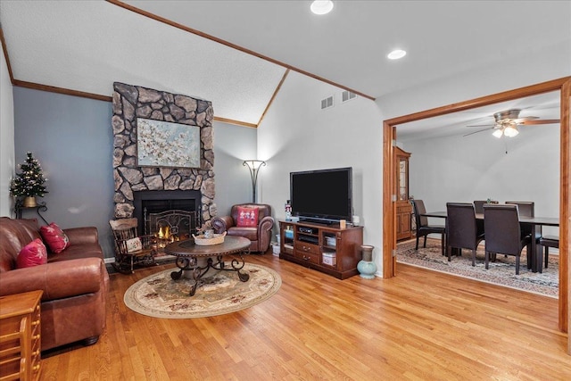 living room with ornamental molding, ceiling fan, wood-type flooring, a stone fireplace, and lofted ceiling