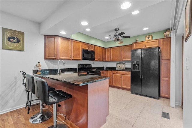 kitchen with ceiling fan, sink, kitchen peninsula, dark stone countertops, and black appliances