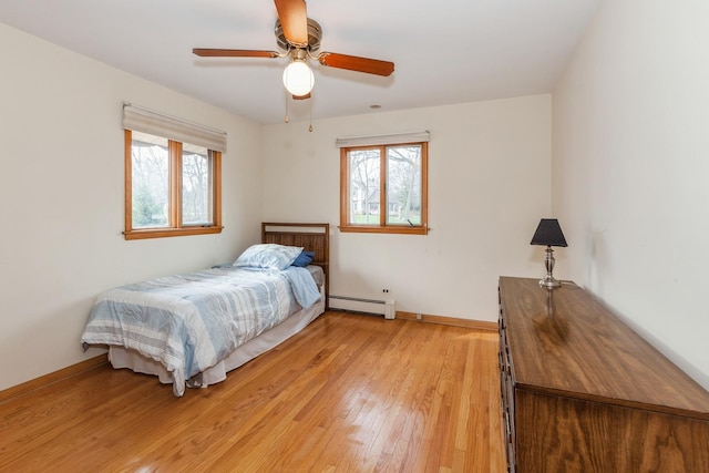 bedroom featuring baseboard heating, multiple windows, baseboards, and light wood-style floors