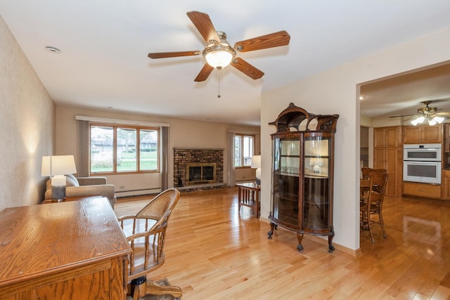 office space featuring baseboards, a fireplace, ceiling fan, light wood-type flooring, and baseboard heating