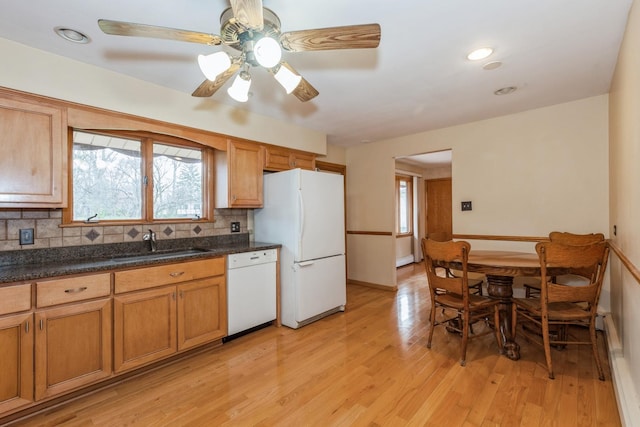 kitchen featuring dark countertops, backsplash, light wood-type flooring, white appliances, and a sink