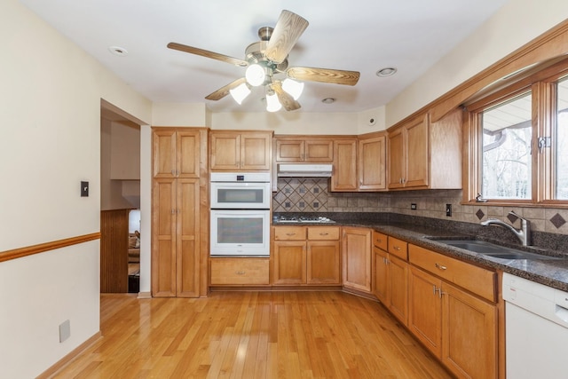 kitchen featuring decorative backsplash, white appliances, light wood-style floors, and a sink