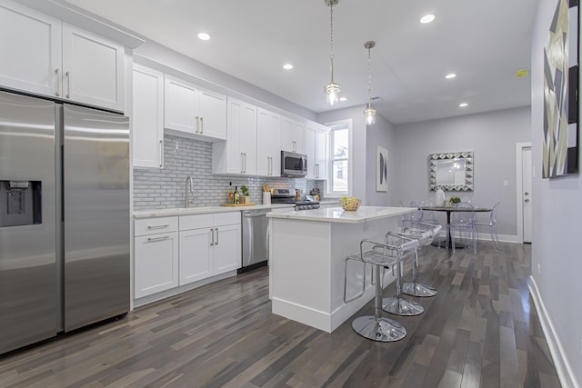 kitchen featuring white cabinetry, hanging light fixtures, stainless steel appliances, dark hardwood / wood-style floors, and a kitchen island