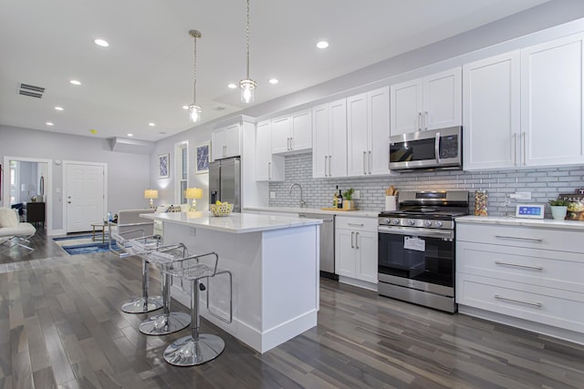 kitchen featuring stainless steel appliances, white cabinetry, hanging light fixtures, and dark wood-type flooring