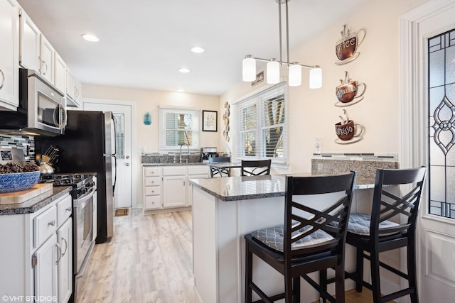 kitchen featuring pendant lighting, white cabinets, light hardwood / wood-style flooring, appliances with stainless steel finishes, and a breakfast bar area