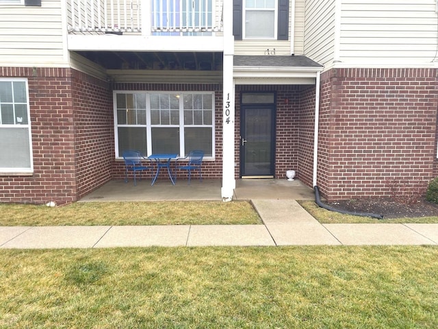 view of exterior entry with a lawn and a balcony