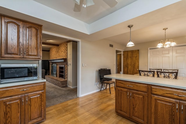 kitchen with a fireplace, light wood-type flooring, ceiling fan with notable chandelier, and hanging light fixtures