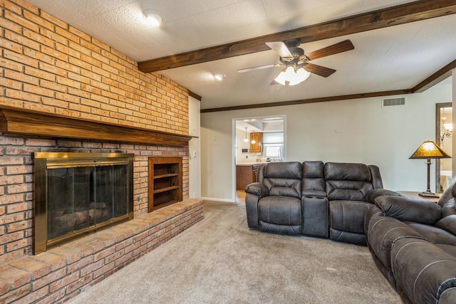 carpeted living room with a brick fireplace, a textured ceiling, ceiling fan, crown molding, and beamed ceiling