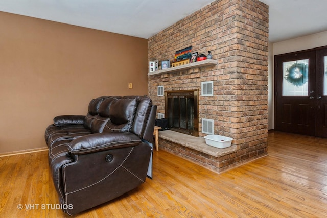 living room featuring french doors, light hardwood / wood-style floors, and a brick fireplace