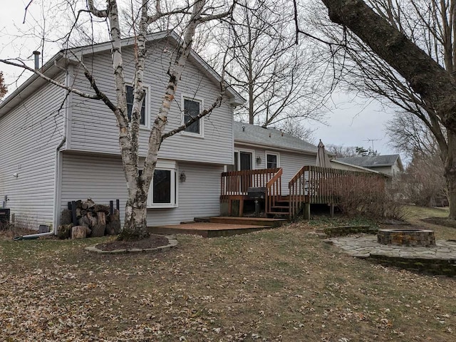 back of house with a deck, an outdoor fire pit, and a lawn