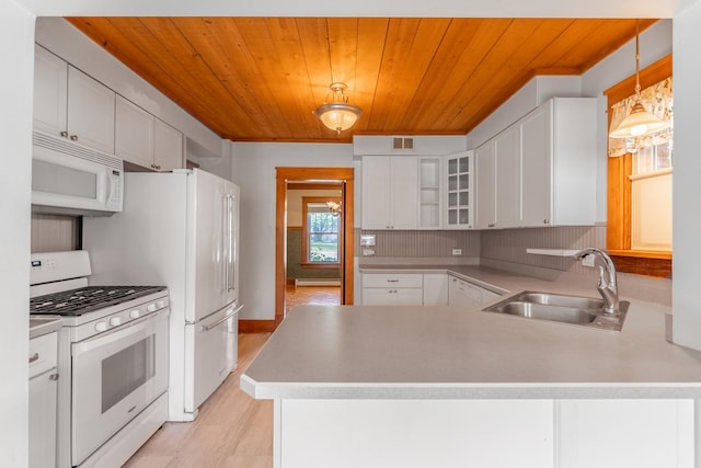 kitchen with kitchen peninsula, white appliances, sink, white cabinets, and hanging light fixtures