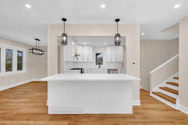 kitchen with light wood-type flooring, white cabinetry, hanging light fixtures, and stainless steel dishwasher