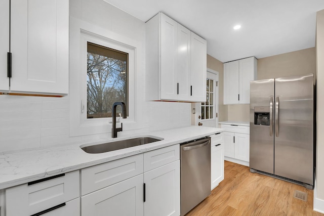 kitchen with sink, light stone counters, appliances with stainless steel finishes, white cabinets, and light wood-type flooring