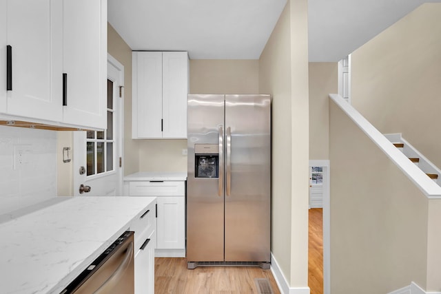 kitchen with white cabinetry, stainless steel appliances, light stone counters, backsplash, and light hardwood / wood-style floors