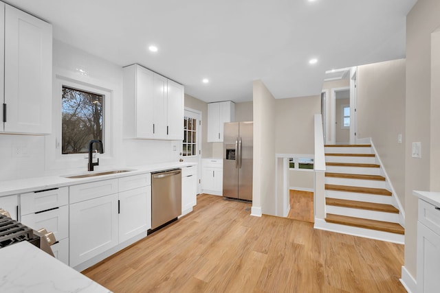 kitchen featuring light stone countertops, white cabinetry, sink, stainless steel appliances, and light wood-type flooring