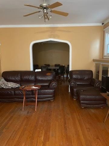 living area featuring a ceiling fan, wood finished floors, arched walkways, and ornamental molding