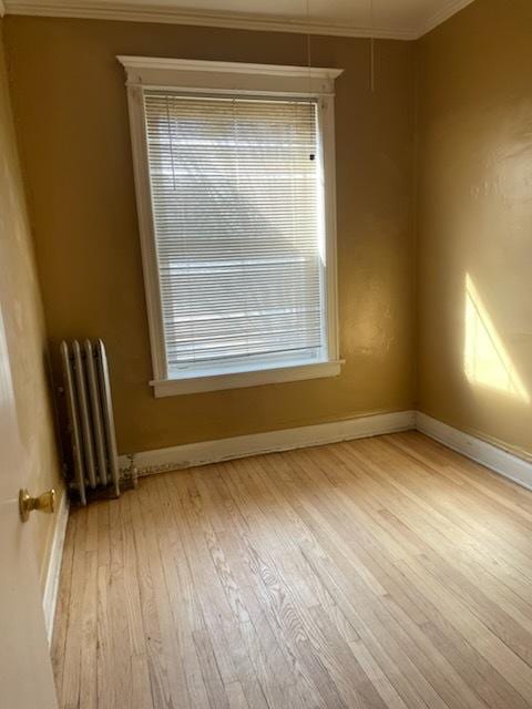 empty room featuring baseboards, wood finished floors, ornamental molding, and radiator heating unit