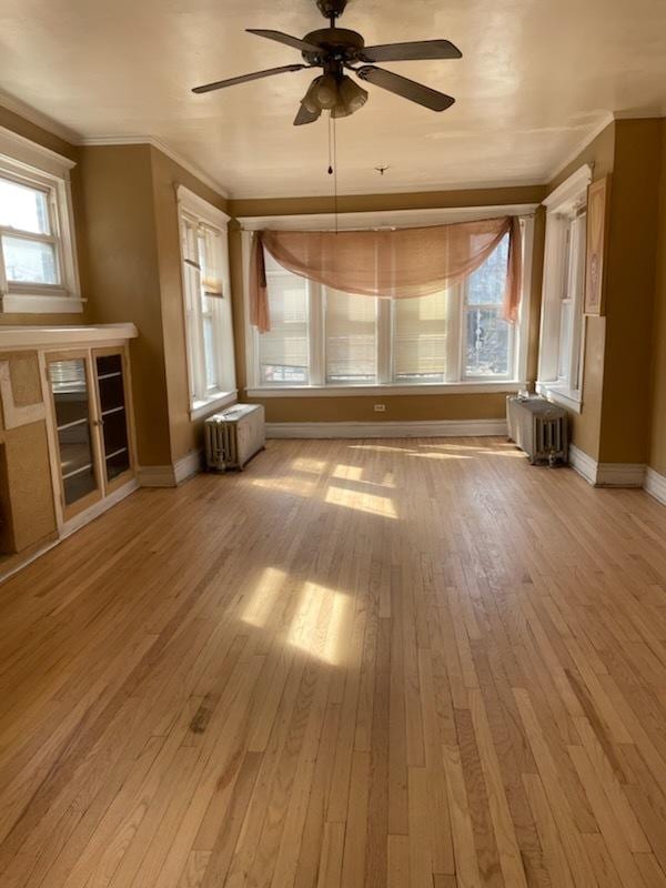 unfurnished living room with radiator heating unit, baseboards, light wood-type flooring, and ornamental molding