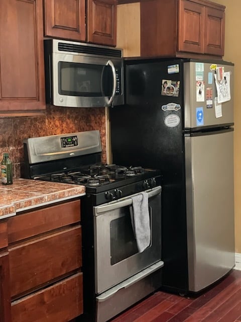 kitchen featuring dark wood-style floors, stainless steel appliances, light countertops, brown cabinets, and backsplash