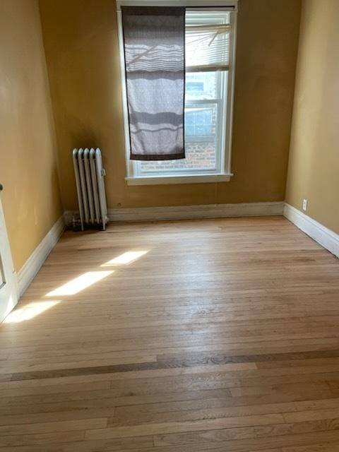 spare room featuring radiator, baseboards, and light wood-style floors