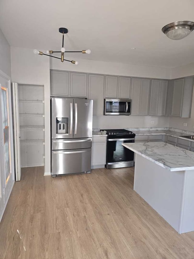 kitchen with light stone countertops, stainless steel appliances, sink, light hardwood / wood-style flooring, and a notable chandelier