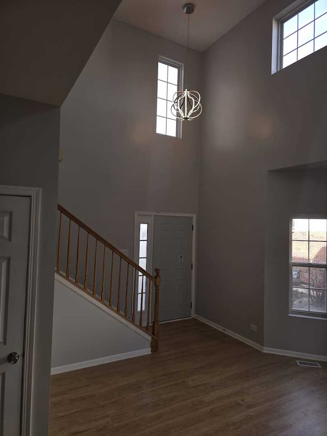 entryway with a chandelier, a towering ceiling, dark hardwood / wood-style floors, and plenty of natural light