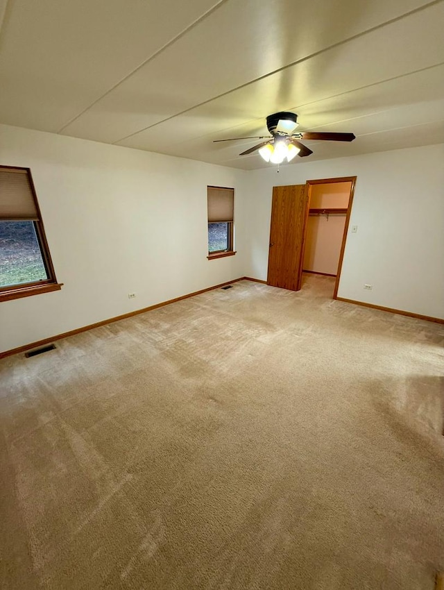 unfurnished bedroom with a closet, a walk in closet, carpet floors, and ceiling fan