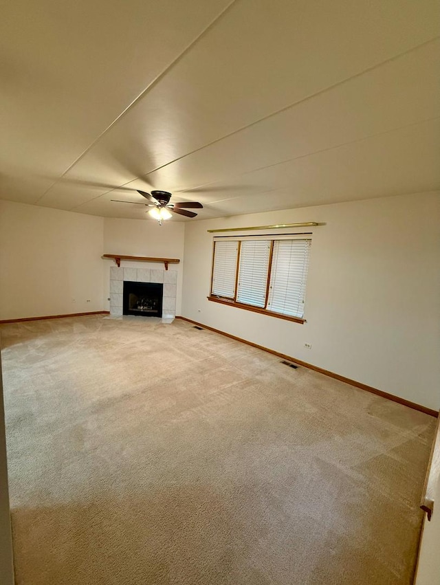 unfurnished living room featuring ceiling fan, carpet floors, and a tiled fireplace