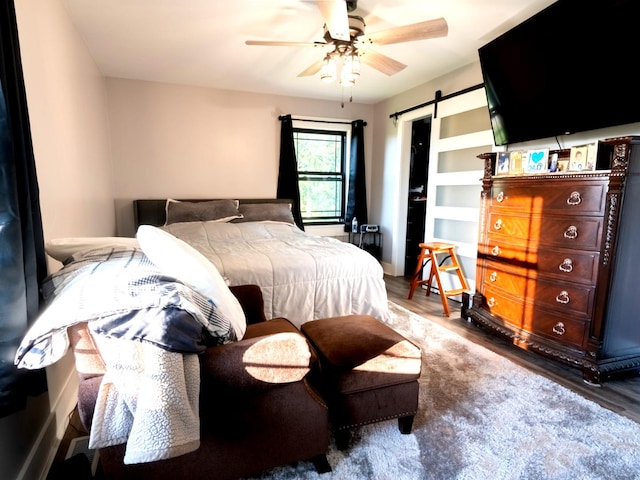 bedroom featuring hardwood / wood-style flooring, ceiling fan, and a barn door