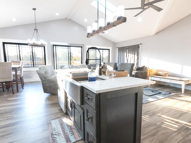 kitchen with dark wood-type flooring, hanging light fixtures, light stone counters, a kitchen island with sink, and ceiling fan with notable chandelier