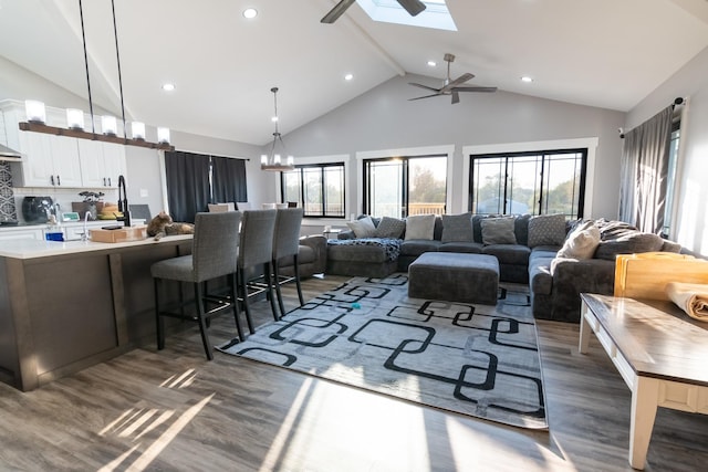 living room with a skylight, ceiling fan with notable chandelier, dark hardwood / wood-style floors, and high vaulted ceiling