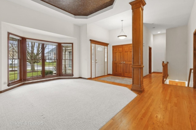 foyer entrance featuring a high ceiling, light wood-type flooring, a tray ceiling, and ornate columns