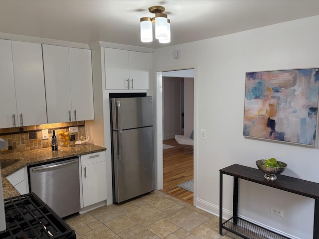 kitchen featuring white cabinets, decorative backsplash, stainless steel appliances, and dark stone countertops