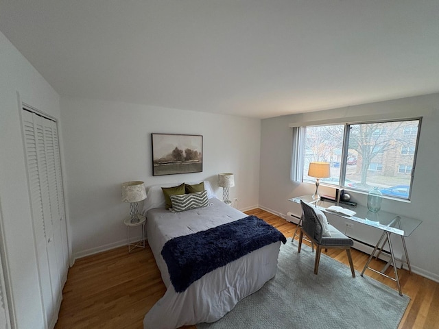 bedroom with hardwood / wood-style floors, baseboard heating, and a closet